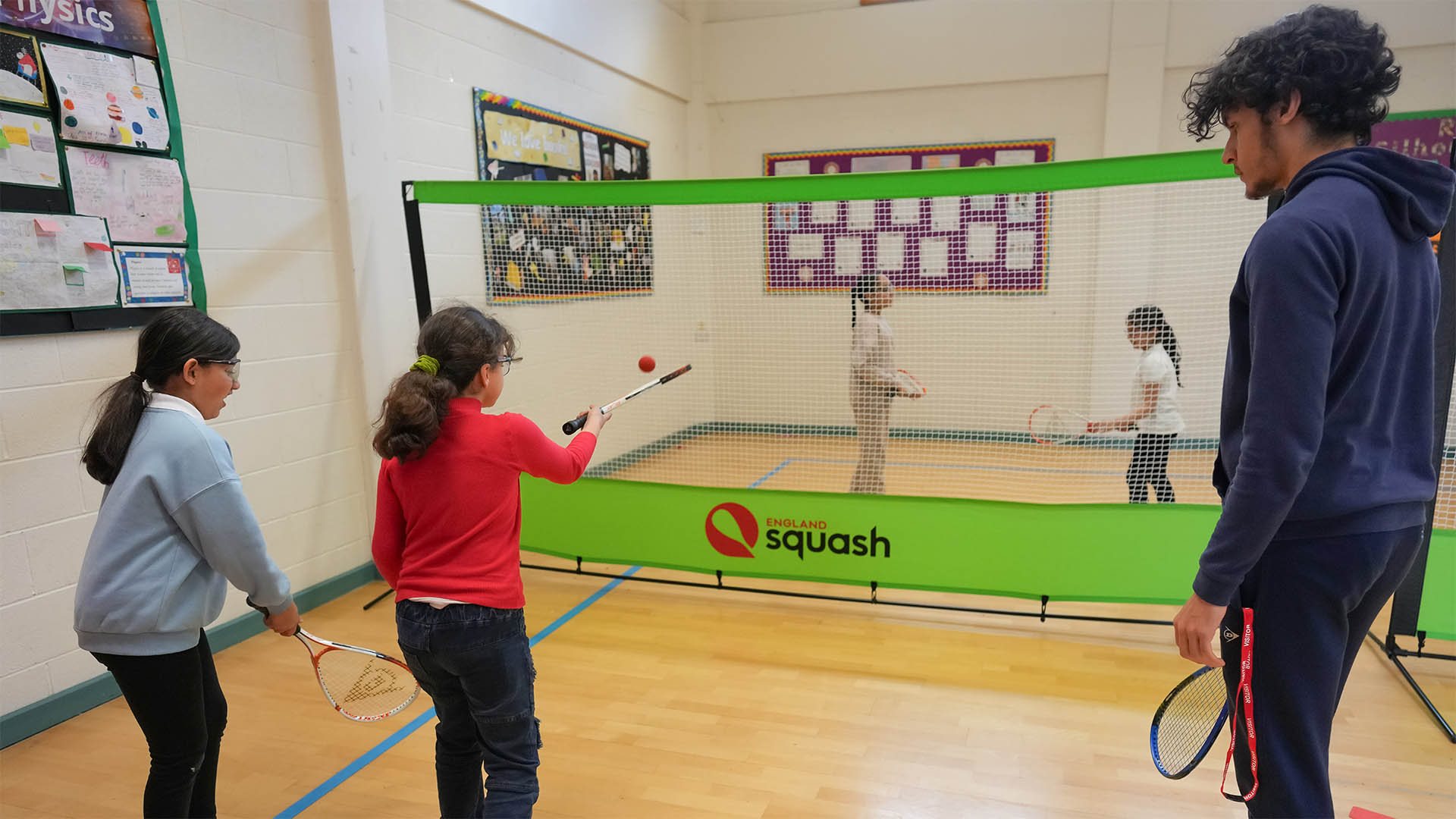 Coach Jules Silvera coaching children squash in a school sports hall